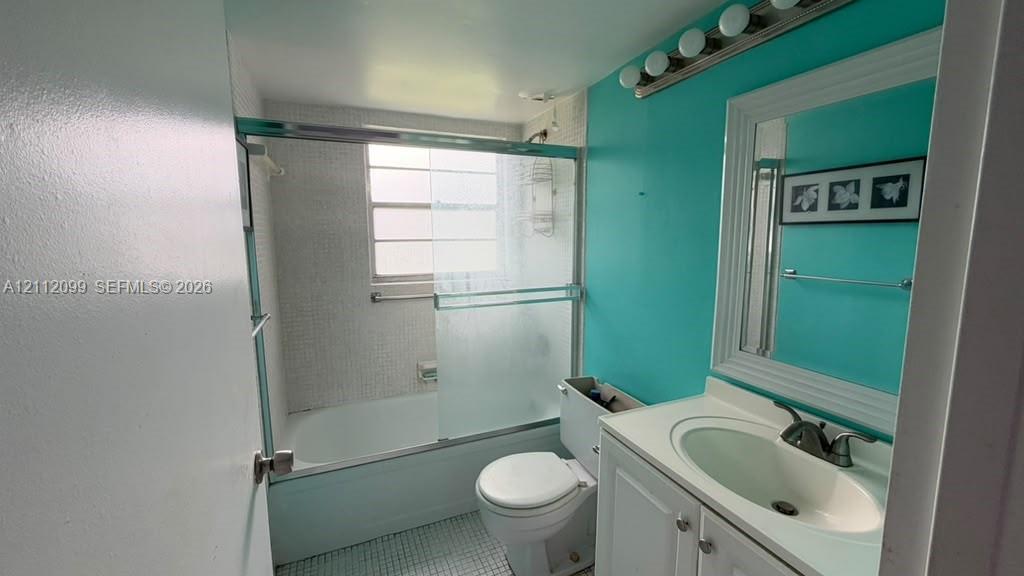 Bathroom featuring a white vanity cabinet with an integrated sink, polished metal faucet, a framed wall mirror, a bathtub with sliding glass doors, and a tiled shower surround