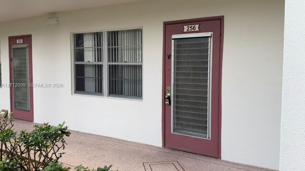 Exterior entrance featuring a solid door with a full-length security screen, dual-pane window with vertical blinds, and a smooth stucco finish