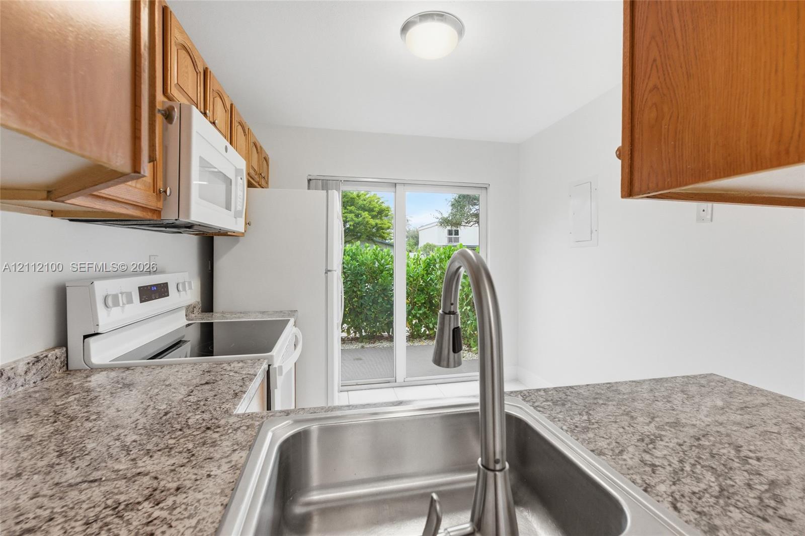 Kitchen featuring speckled laminate countertops, stainless steel undermount sink with a high-arch pull-down faucet, wood-finish cabinetry, white appliances, and a glass sliding door