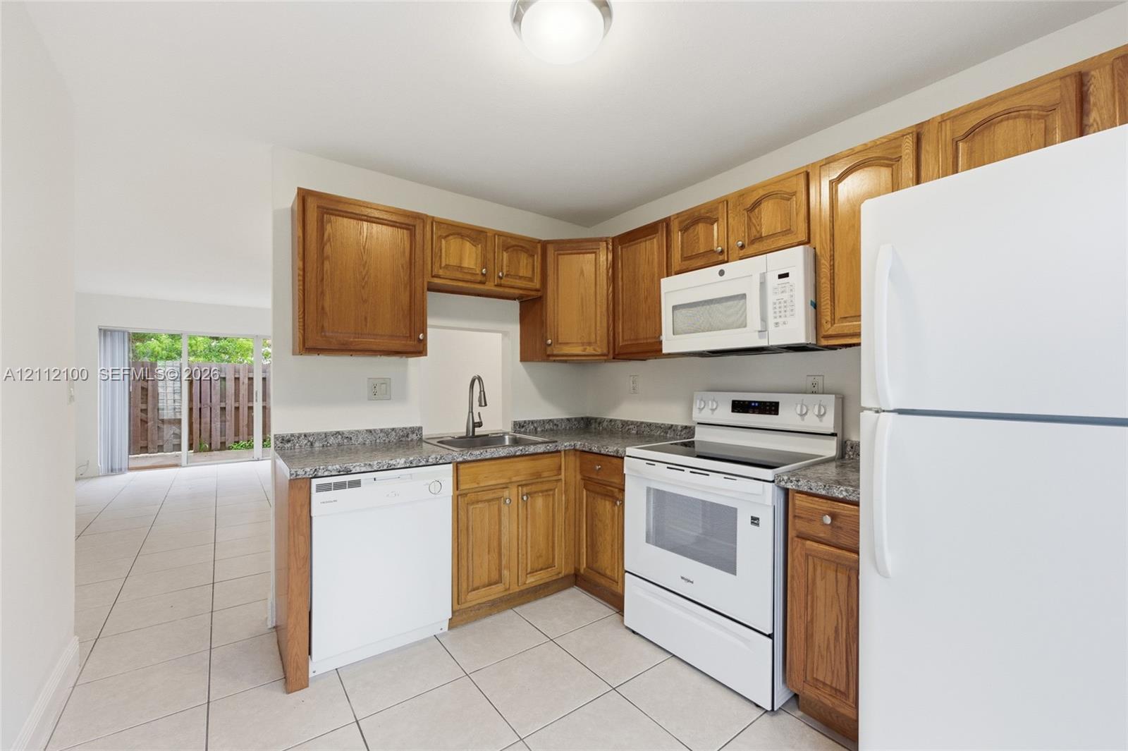 Kitchen featuring wood cabinetry, stone-patterned laminate countertops, tile flooring, and white appliances including a range, microwave, and dishwasher
