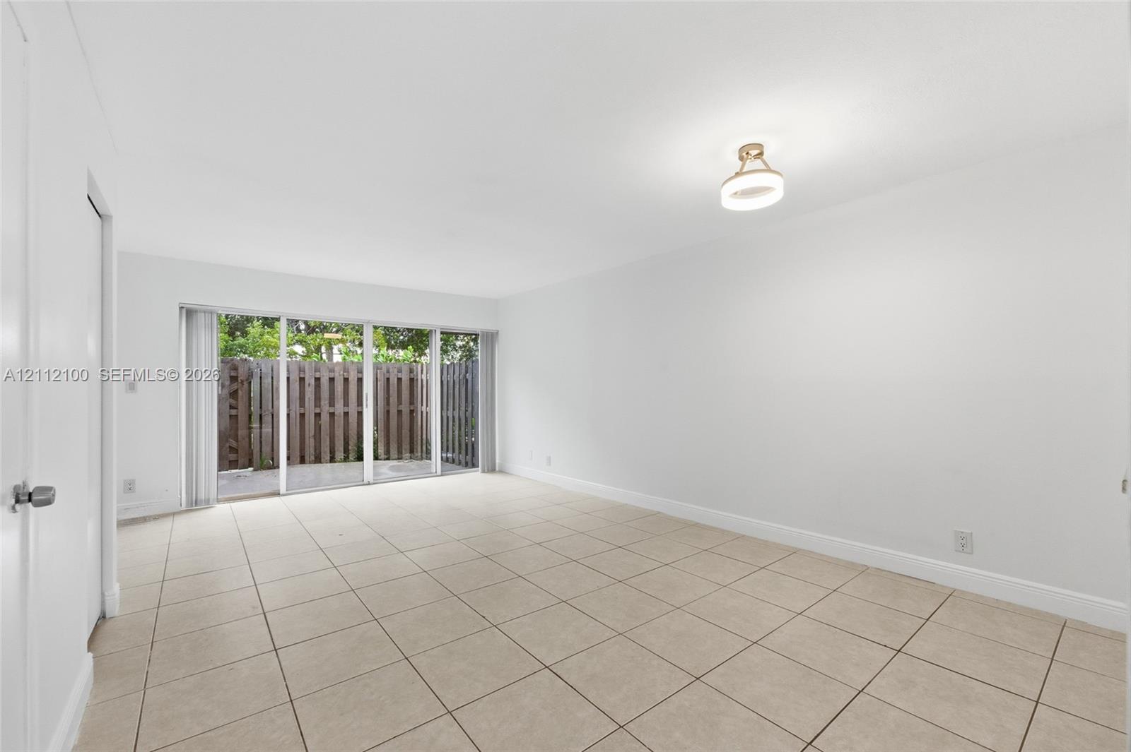 Neutral-toned tile flooring, flush-mount circular ceiling lighting, and expansive floor-to-ceiling glass sliding doors opening to a fenced exterior area
