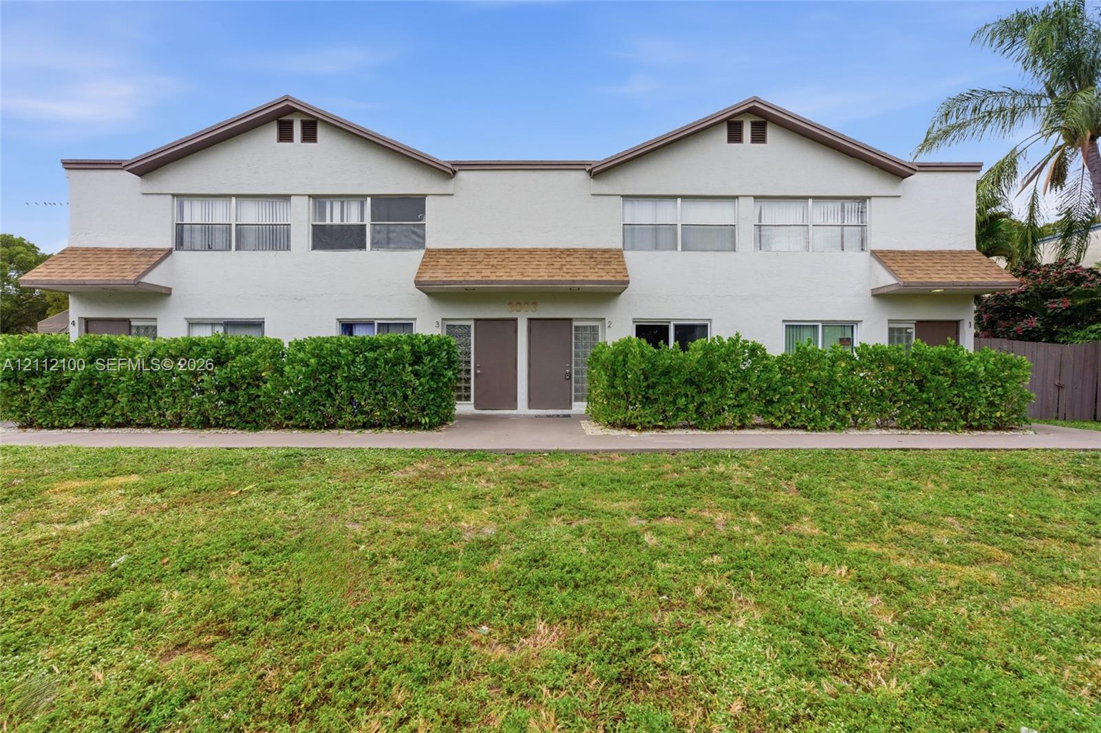 Two-story multi-unit exterior featuring stucco siding, gabled roof lines, shingle accents, horizontal sliding windows, and a concrete walkway