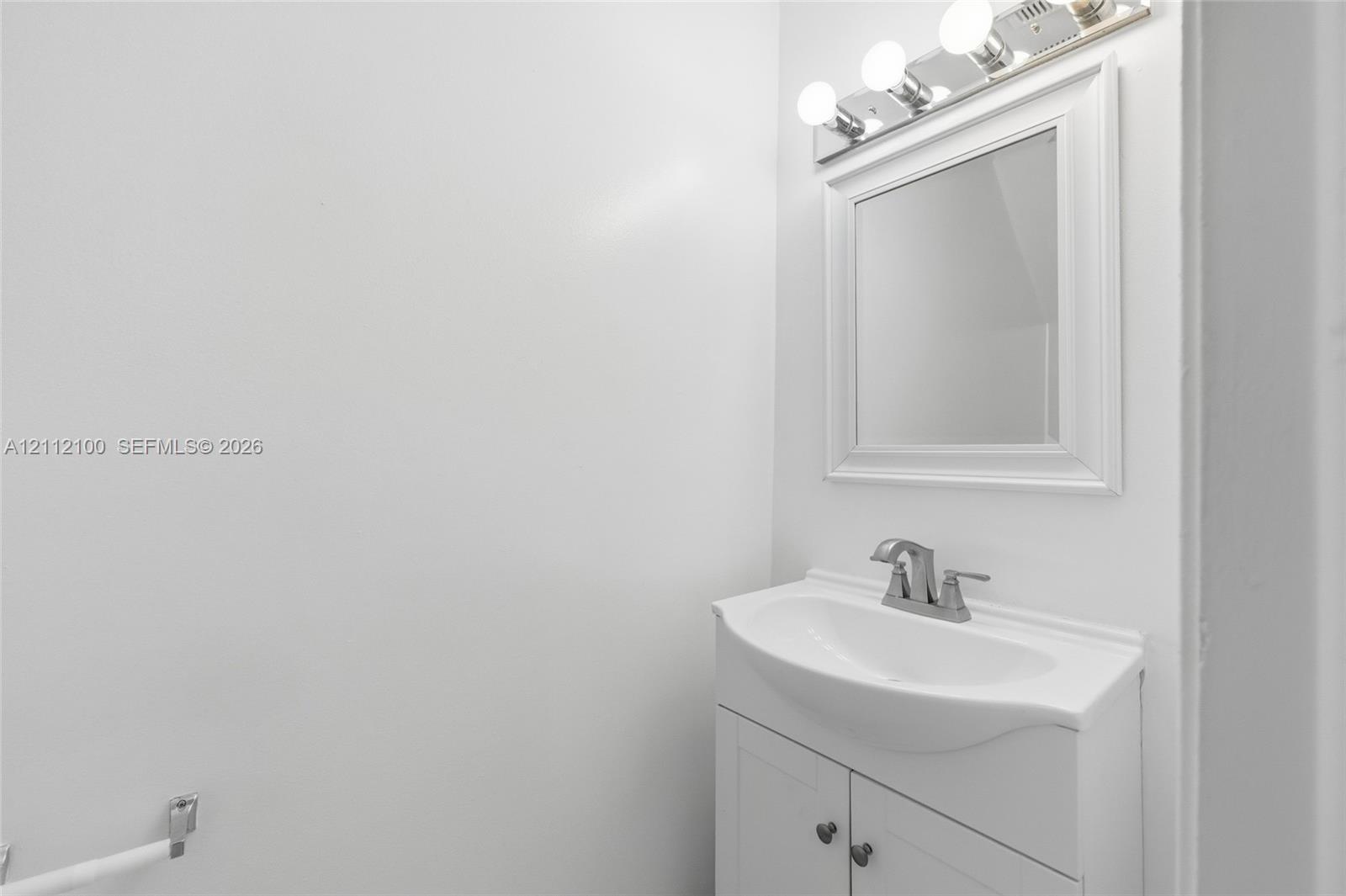 White vanity with an integrated sink, polished metal faucet, matching framed mirror, and multi-bulb vanity light fixture