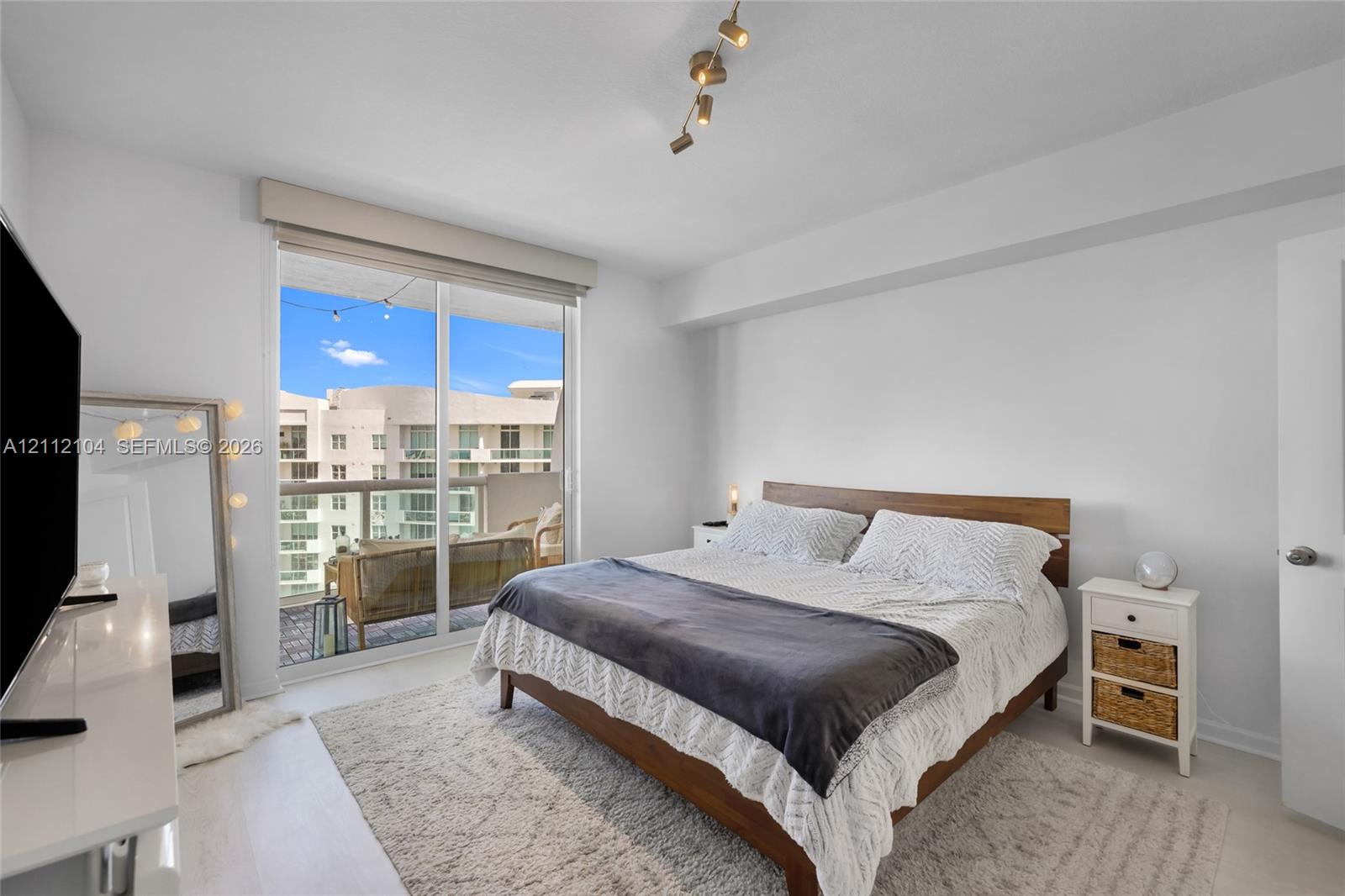 Sliding glass door opening to a private balcony, wood-finish flooring, and adjustable multi-bulb track lighting