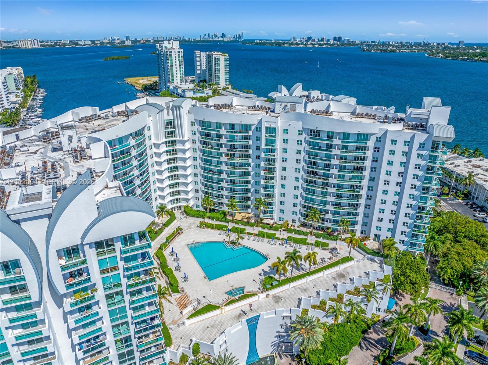 High-rise residential exterior featuring expansive glass balconies, an outdoor swimming pool, manicured landscaping, and direct waterfront access
