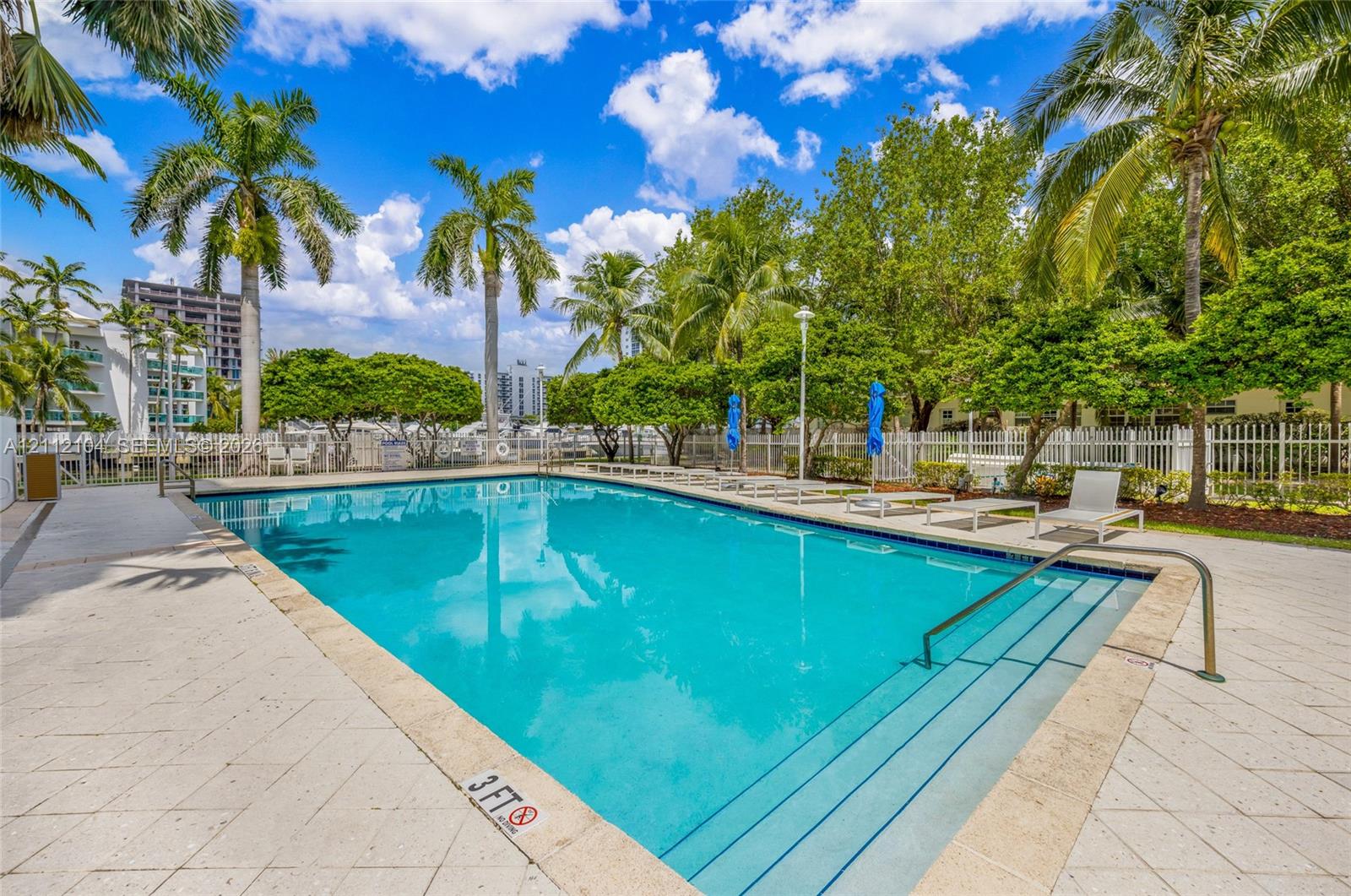 In-ground swimming pool featuring a light-toned stone deck, built-in entry steps, stainless steel handrail, and surrounding mature palm trees