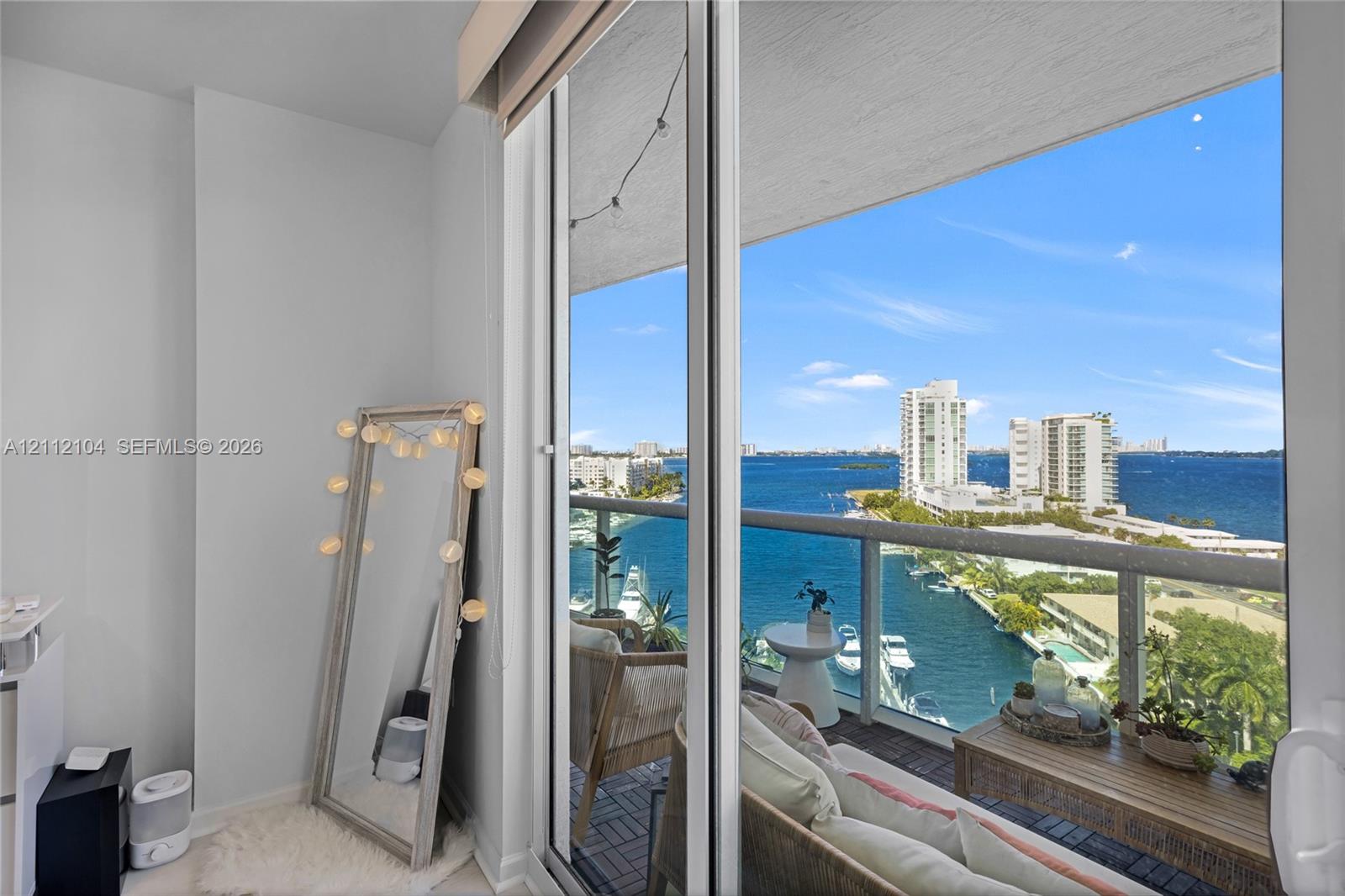 Full-height sliding glass doors opening to a private balcony with a metal and glass railing and expansive water, marina, and city skyline scenery