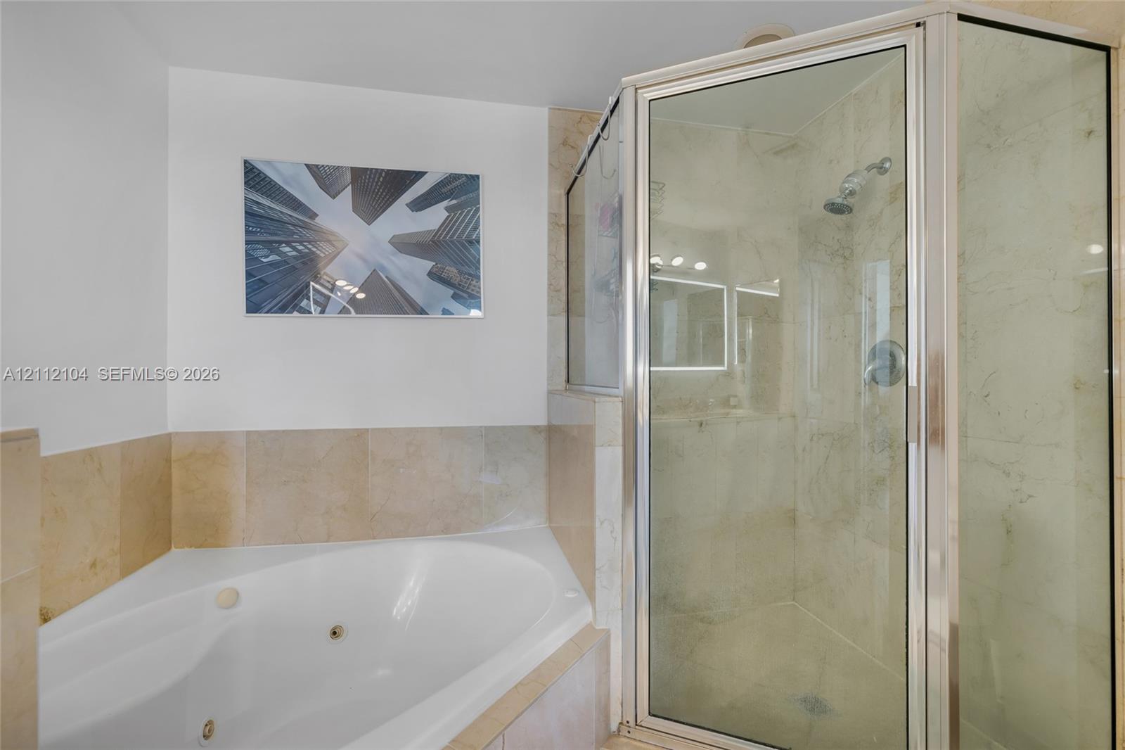 Corner jetted soaking tub with tile surround, glass-enclosed shower featuring tile walls, and polished metal hardware