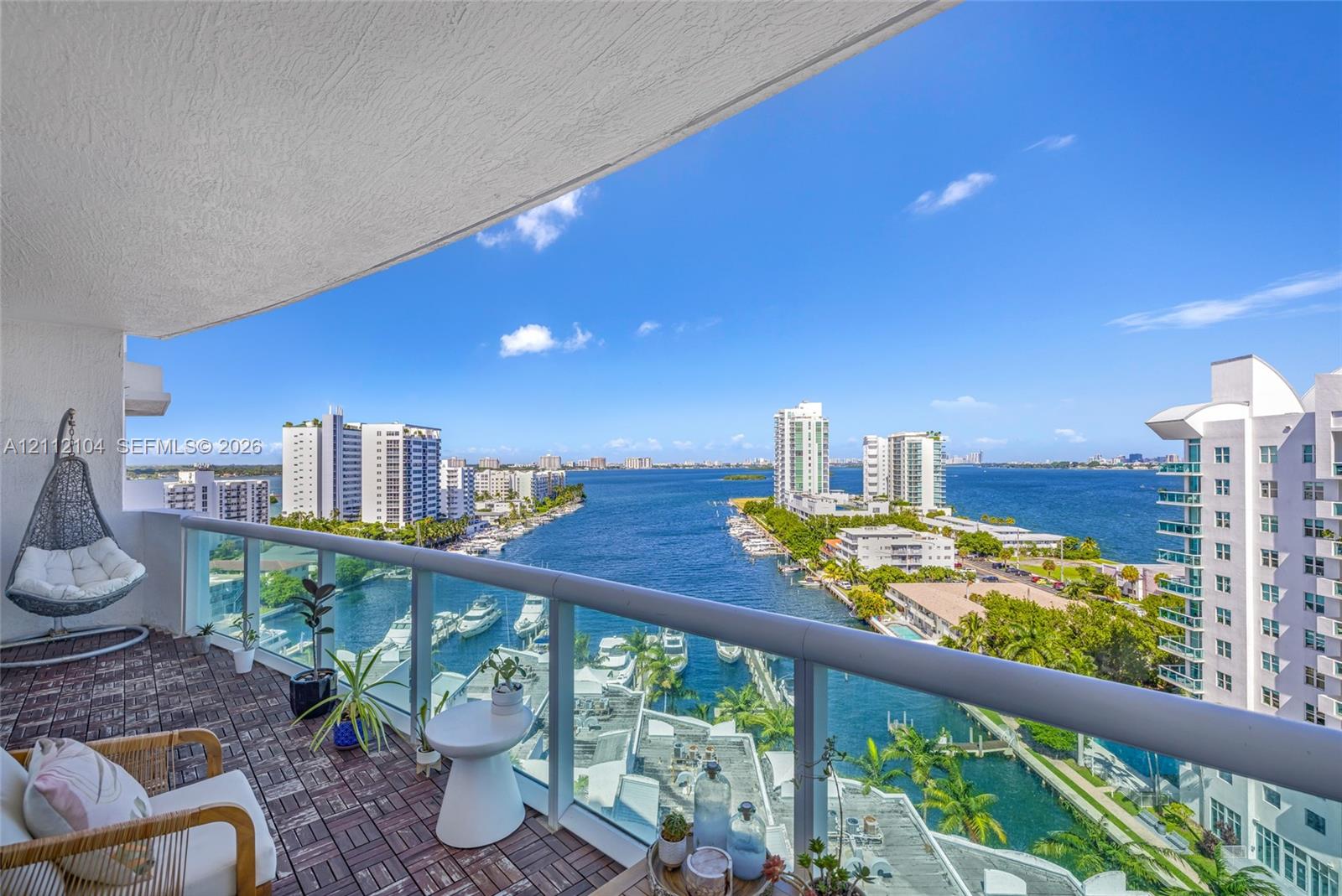 Covered balcony featuring wood-finish decking and a glass-paneled railing overlooking the waterway