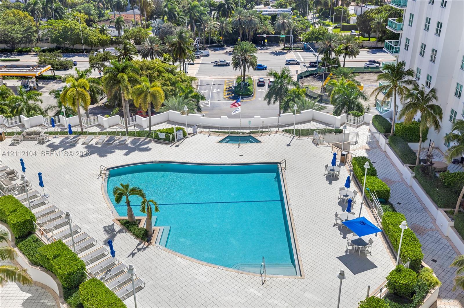 Swimming pool with integrated spa, surrounded by expansive paved decking and manicured privacy hedging