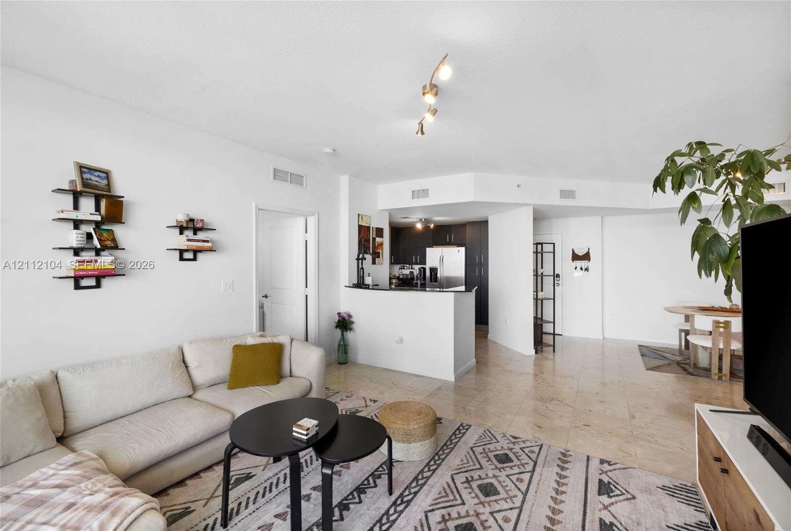 Open-concept interior featuring large-format tile flooring, recessed and track lighting, and a kitchen peninsula with a dark countertop