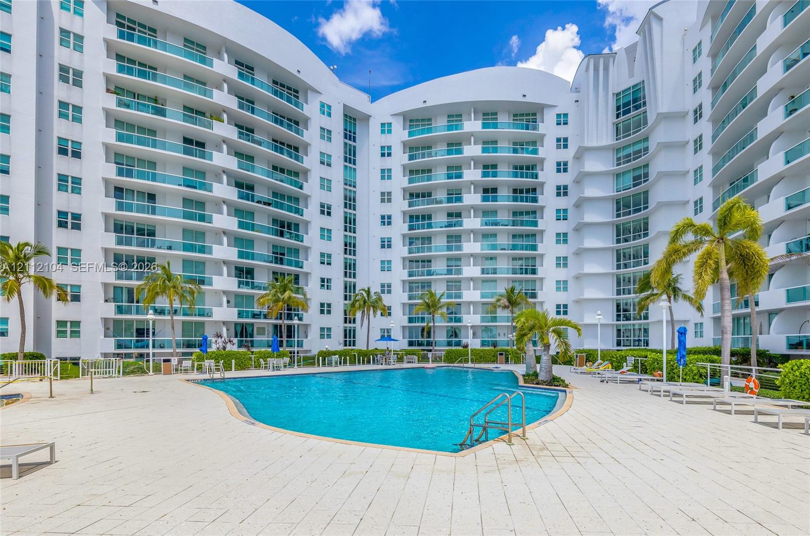 Community swimming pool featuring a paved deck and manicured perimeter landscaping