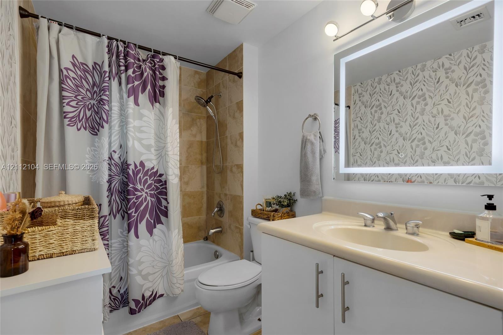 Bathroom featuring a bathtub with tile surround, vanity with an integrated sink and countertop, backlit vanity mirror, and three-light vanity fixture