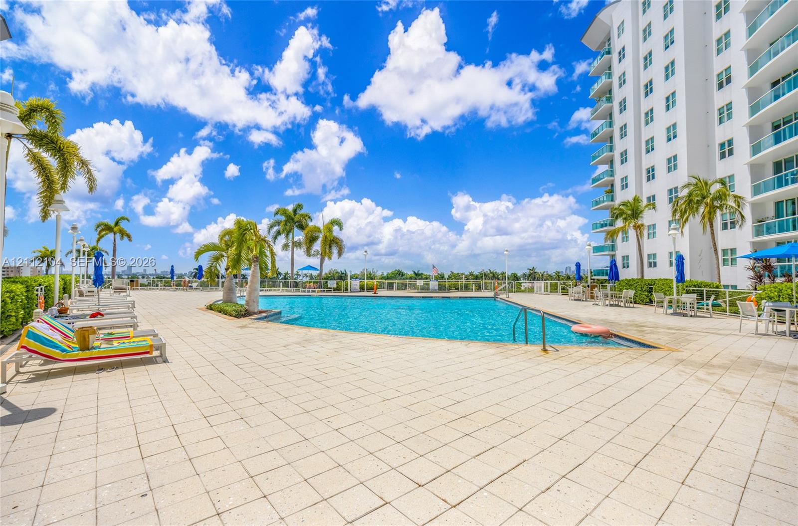 Swimming pool with tiled decking, mature palm trees, and perimeter fencing