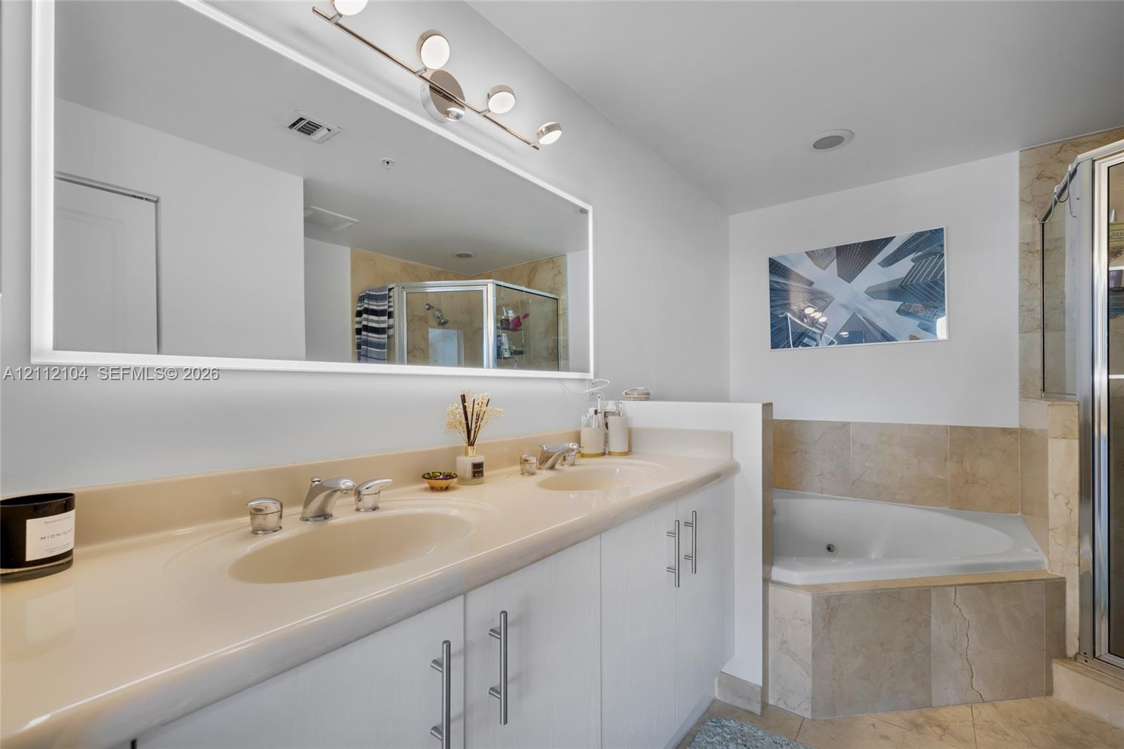 Dual-sink vanity with a seamless countertop, large wall-mounted mirror, multi-light fixture, corner soaking tub, and stone-tile surround