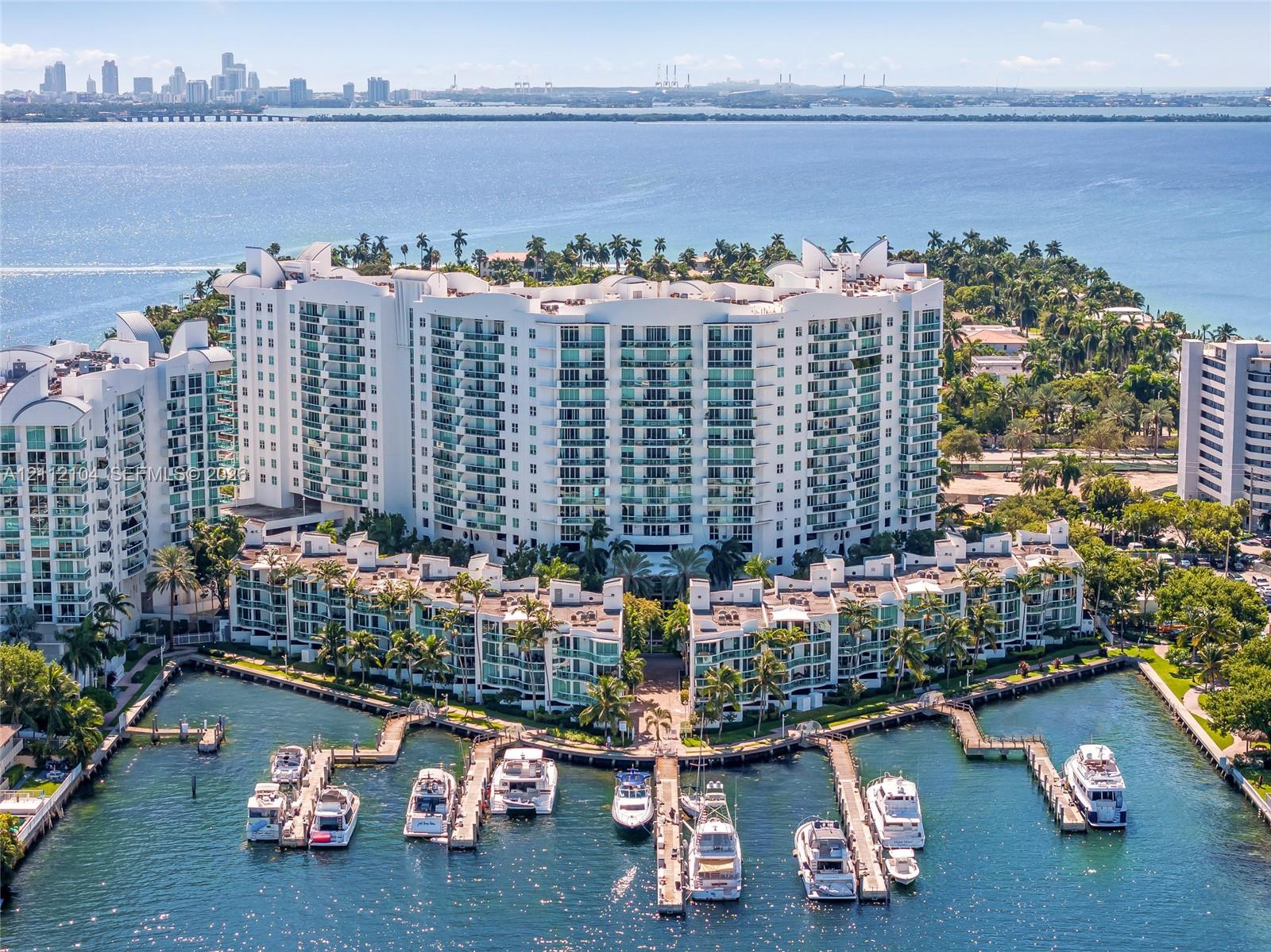 Waterfront condominium complex featuring high-rise architecture, private boat slips, balconies with glass railings, landscaped grounds, and a cityscape backdrop