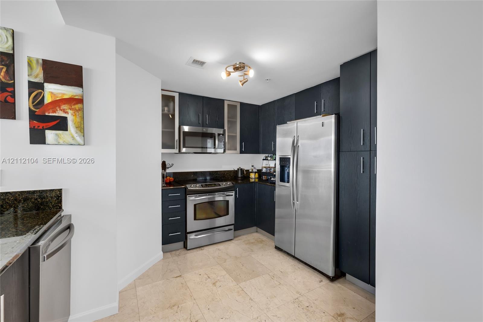 Kitchen featuring dark-stained cabinetry, stone-surface countertops, stainless steel appliances, and natural stone flooring