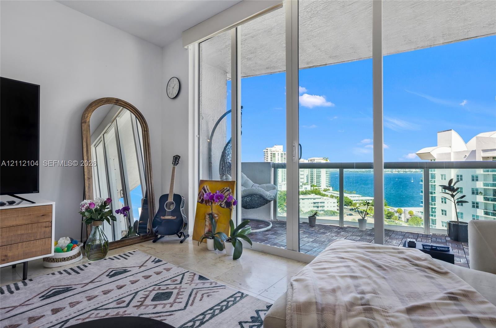 Floor-to-ceiling sliding glass doors opening to a private balcony with glass railing, stone flooring, and water frontage