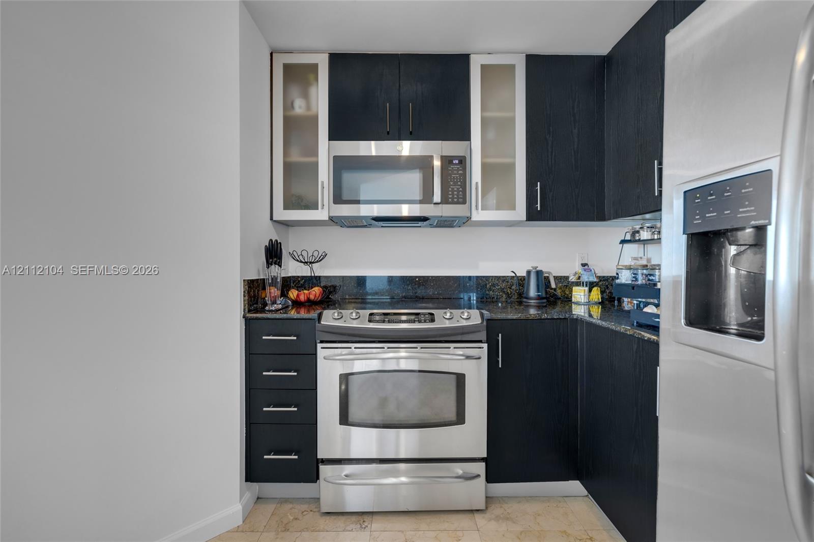 Kitchen featuring dark wood-finish cabinetry, glass-panel upper cabinets, stainless steel appliances, and dark stone-finish countertops