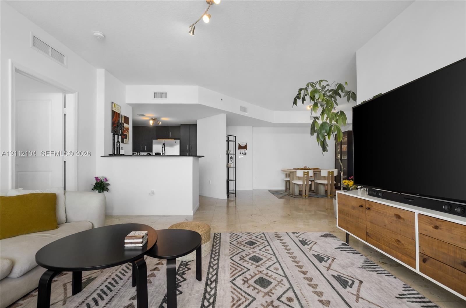 Open-concept interior featuring light-toned tile flooring, recessed ceiling lighting, and a kitchen peninsula with a dark countertop