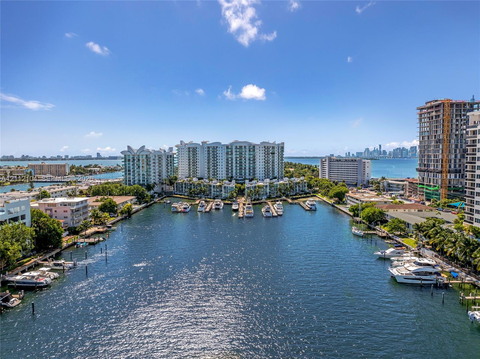 Aerial waterway perspective featuring a deep-water canal, private marina slips, coastal residential buildings, and distant urban skyline