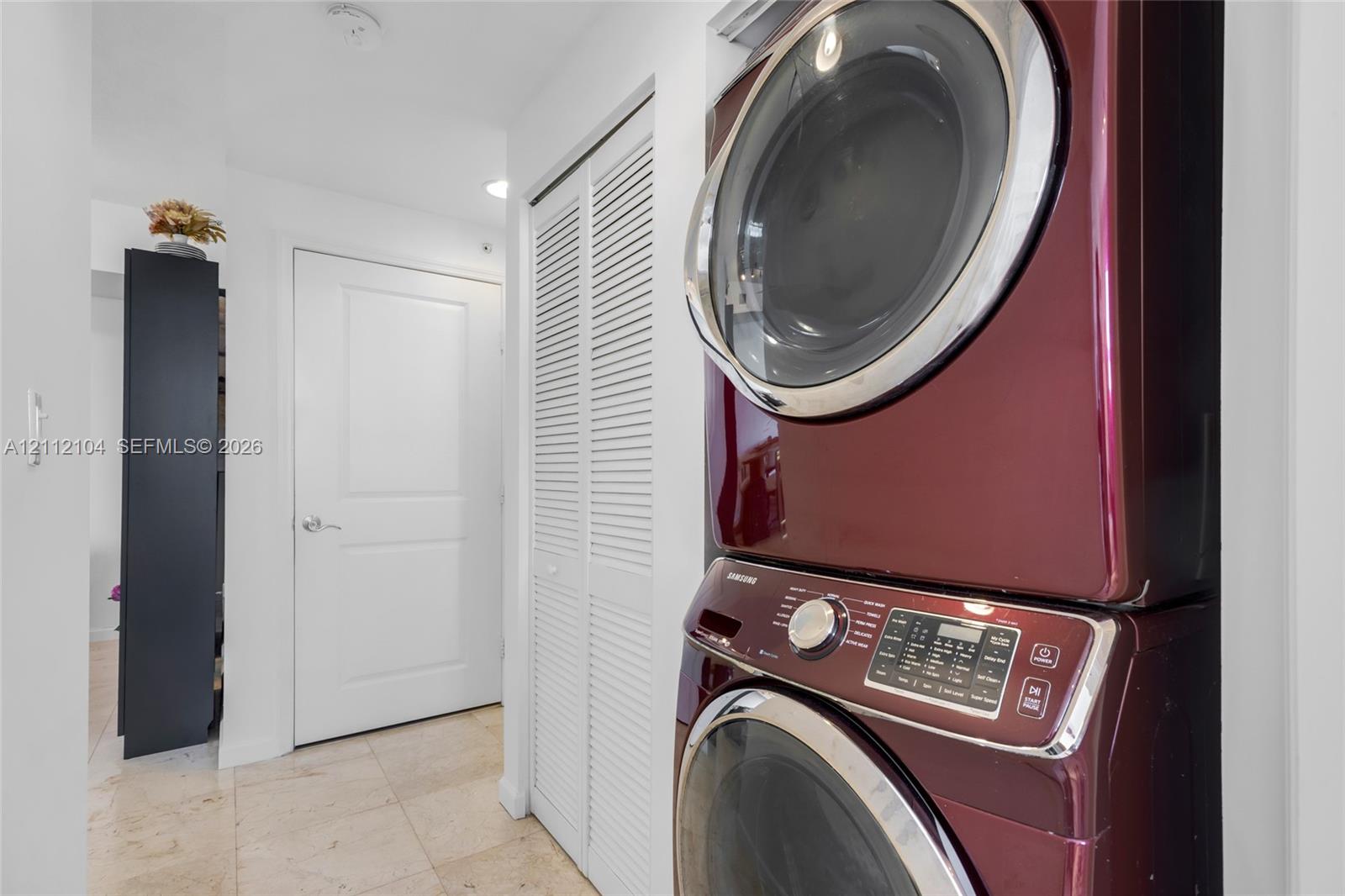 Laundry closet featuring a stackable washer and dryer set, white louvered doors, and stone-finish flooring