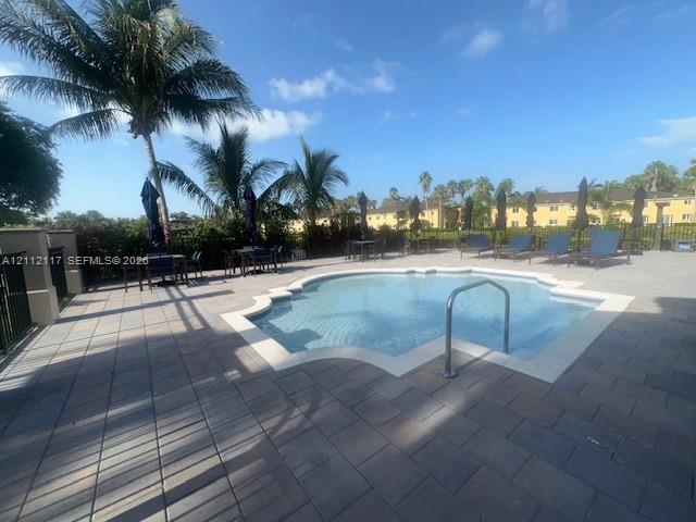 Swimming pool featuring a concrete paver deck, metal pool ladder, and surrounding palm trees