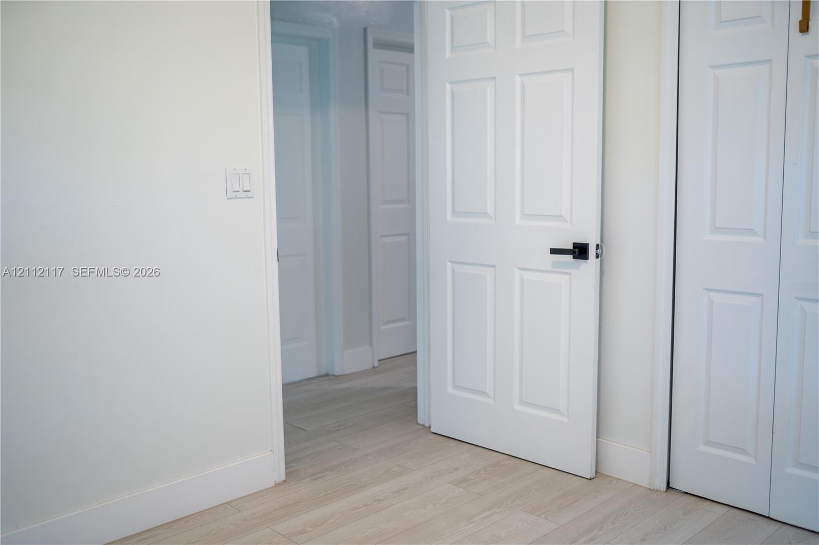 Interior space featuring light wood-finish flooring, six-panel interior doors, and matte black hardware