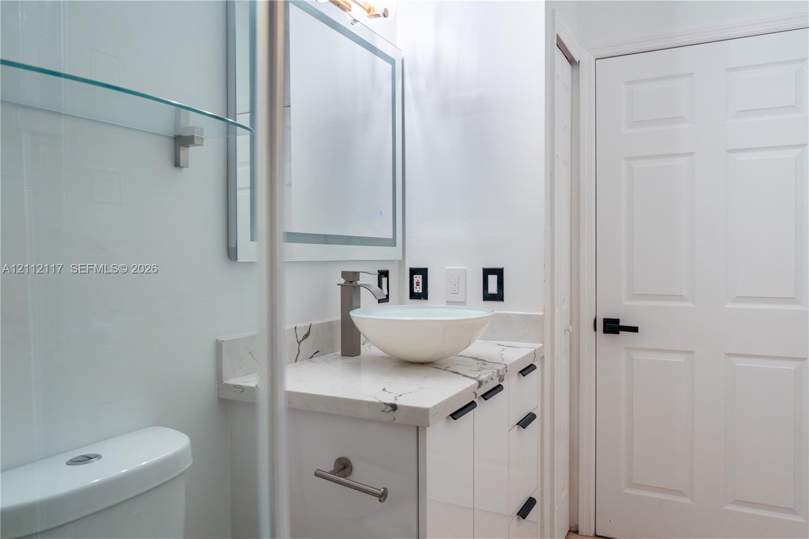 Bathroom vanity featuring a stone-surface countertop, vessel sink, high-profile faucet, and integrated mirror with perimeter lighting
