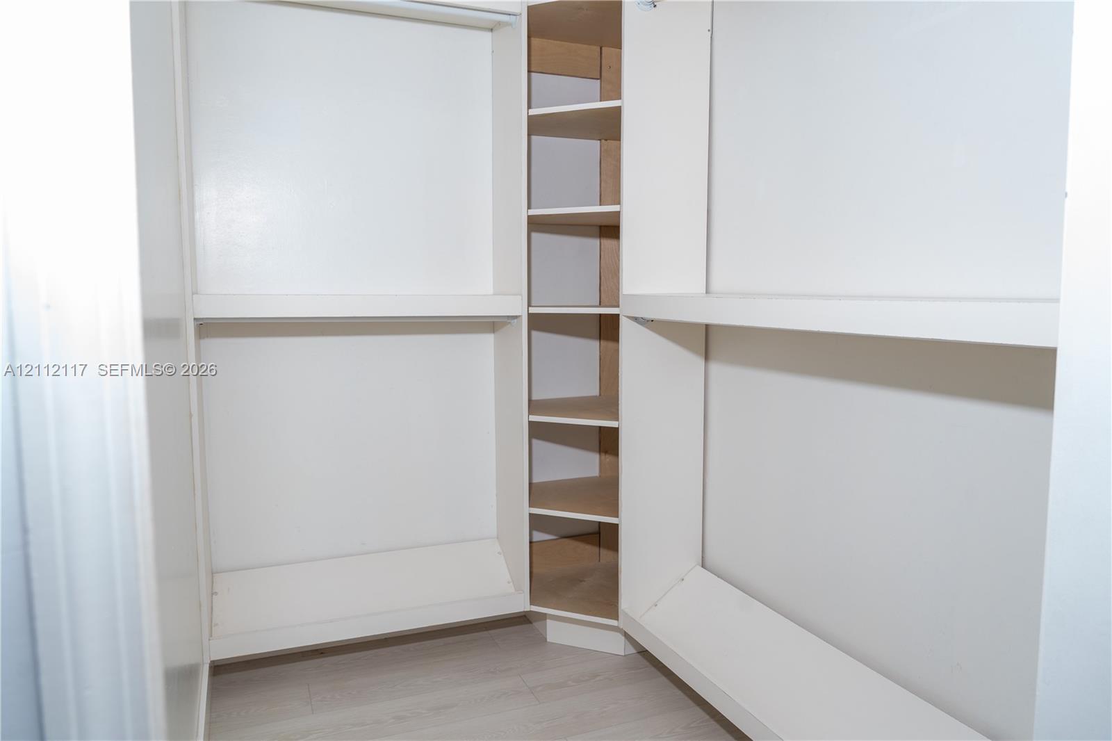 Storage area featuring white built-in shelving and wood-finish flooring Storage area featuring white built-in shelving and wood-finish flooring