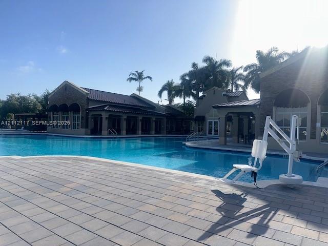 Large outdoor swimming pool featuring paver stone decking, covered patio areas, and structural masonry exteriors