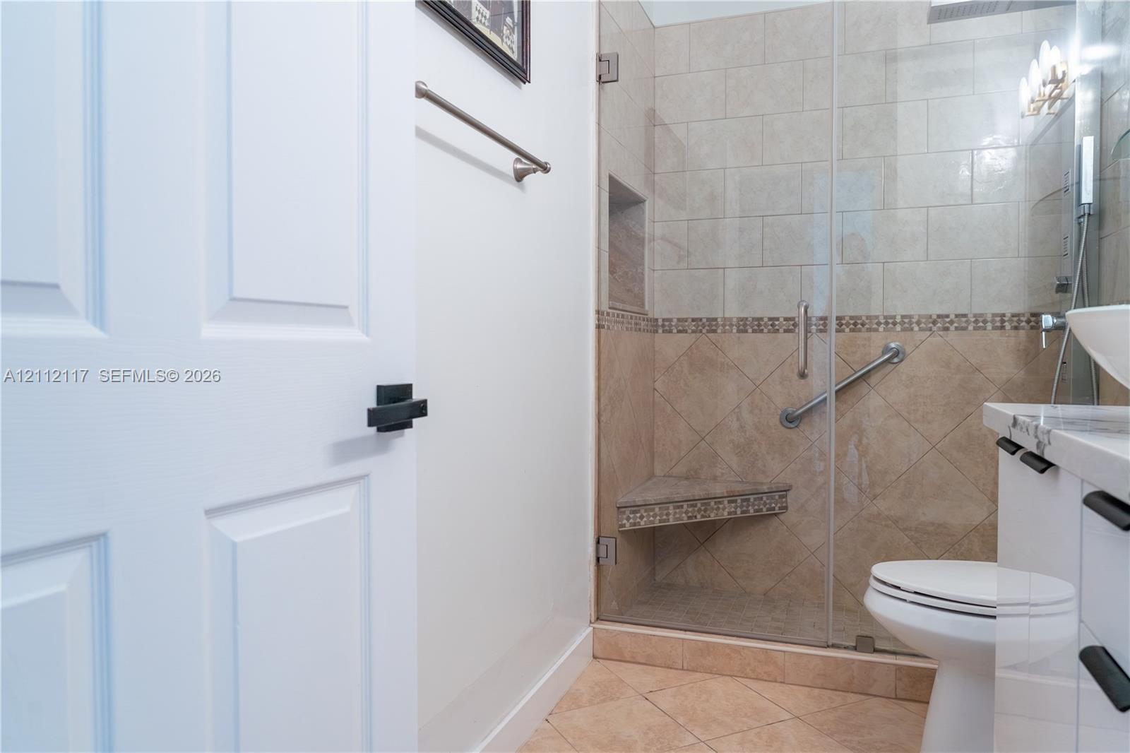 Walk-in shower with frameless glass door, tile surround, built-in corner bench, and recessed wall niche, paired with a white vanity featuring a stone countertop and rectangular vessel sink