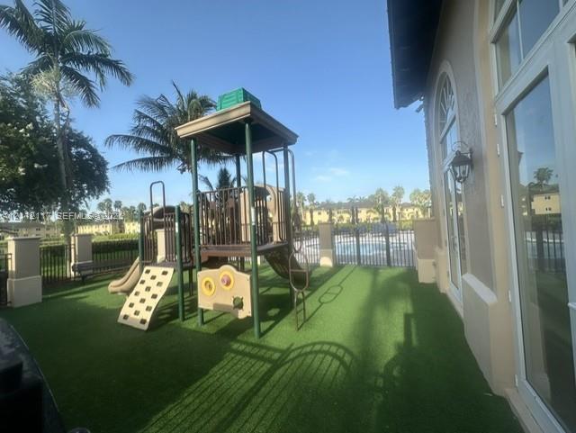 Outdoor space featuring synthetic turf, fixed play structure, arched glass-paned double doors, and exterior wall-mounted light fixtures