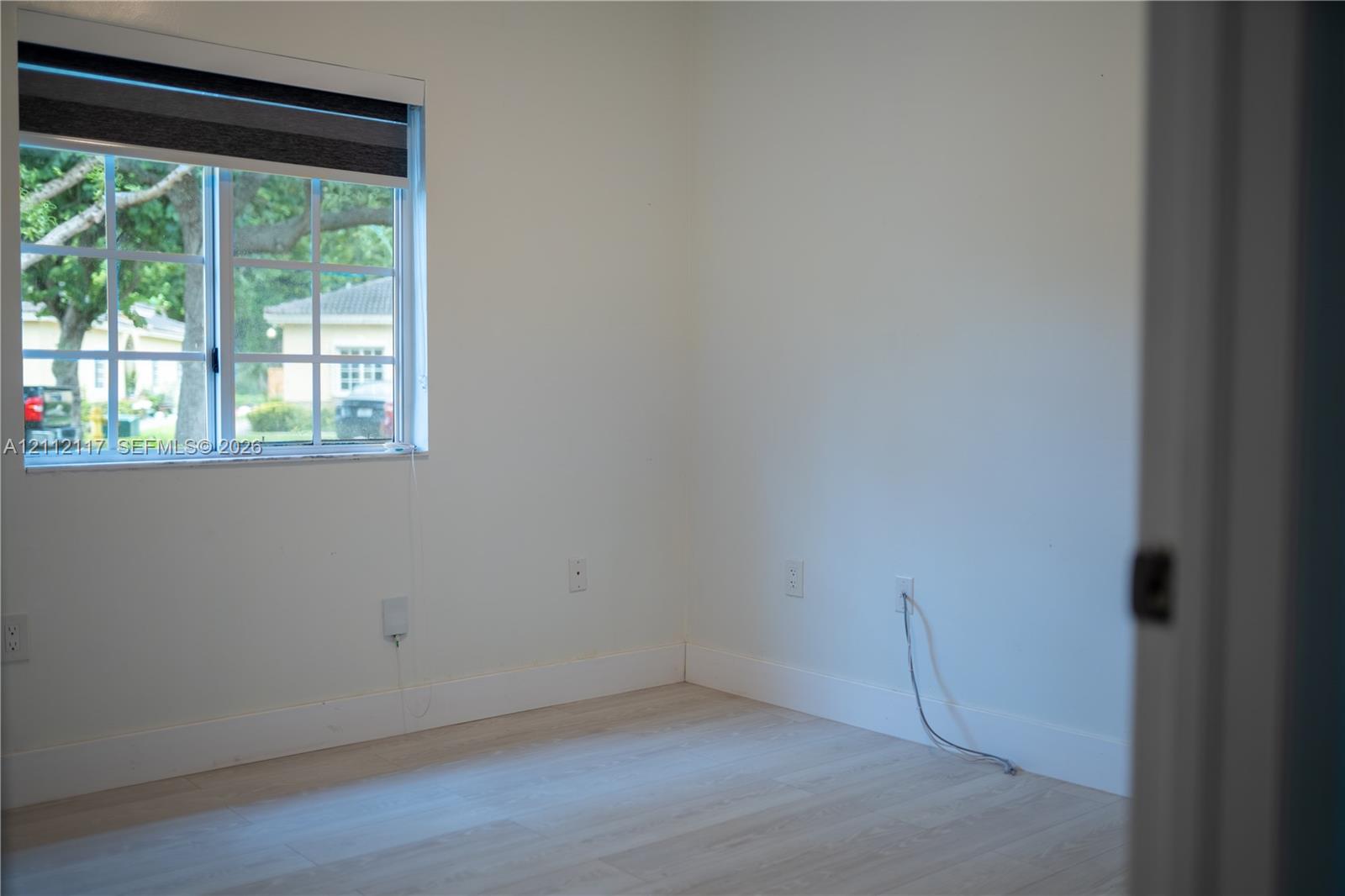 Neutral-toned interior room featuring wood-finish flooring and a multi-pane window with a roller shade