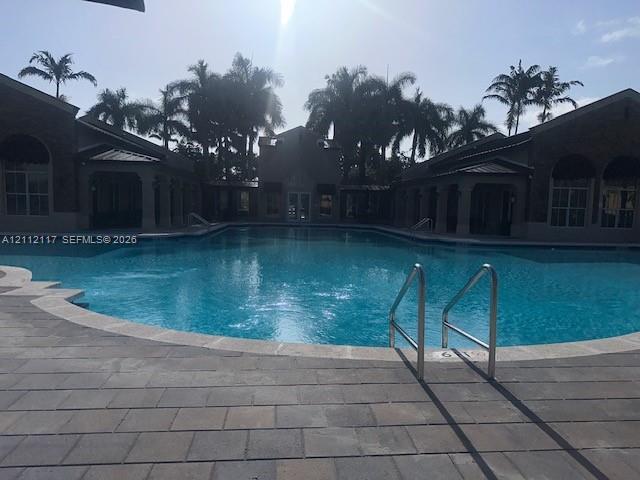 In-ground swimming pool featuring stone paver decking, metal railings, and an expansive courtyard surrounded by palm trees