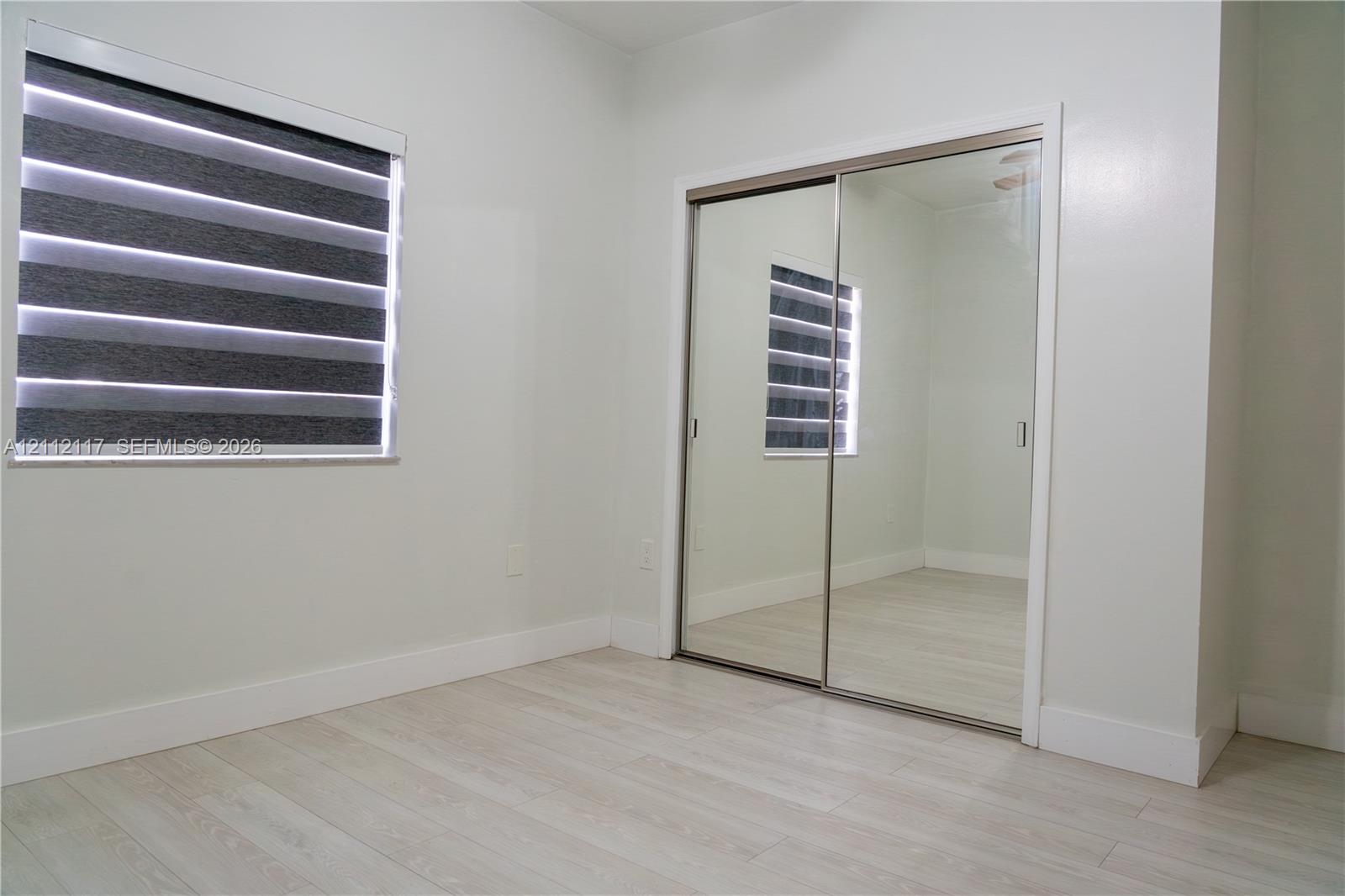 Light-toned wood-finish flooring, dual-panel mirrored sliding closet doors, and multi-layered fabric window blinds