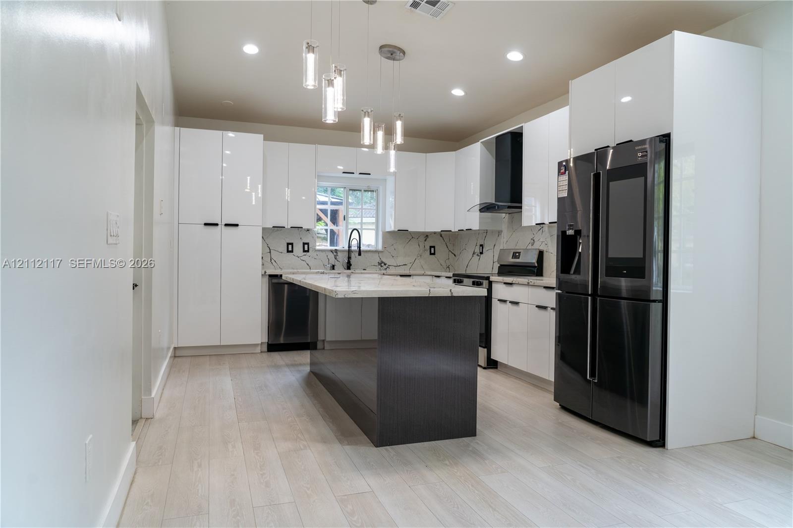 Kitchen featuring high-gloss white cabinetry, a center island with a dark finish, stone-patterned countertops, a stainless steel appliance package, and modern glass pendant lighting Kitchen featuring high-gloss white cabinetry, a center island with a dark finish, stone-patterned countertops, a stainless steel appliance package, and modern glass pendant lighting