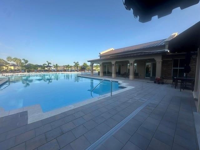 In-ground swimming pool featuring a tiled deck, covered patio, metal roof, and stone masonry exterior accents