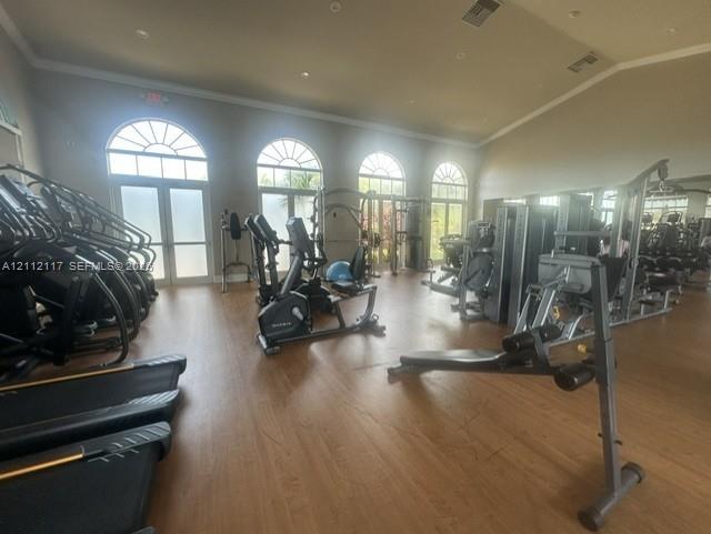 Fitness facility featuring arched windows, vaulted ceilings, wood-finish flooring, and wall-to-wall mirrors