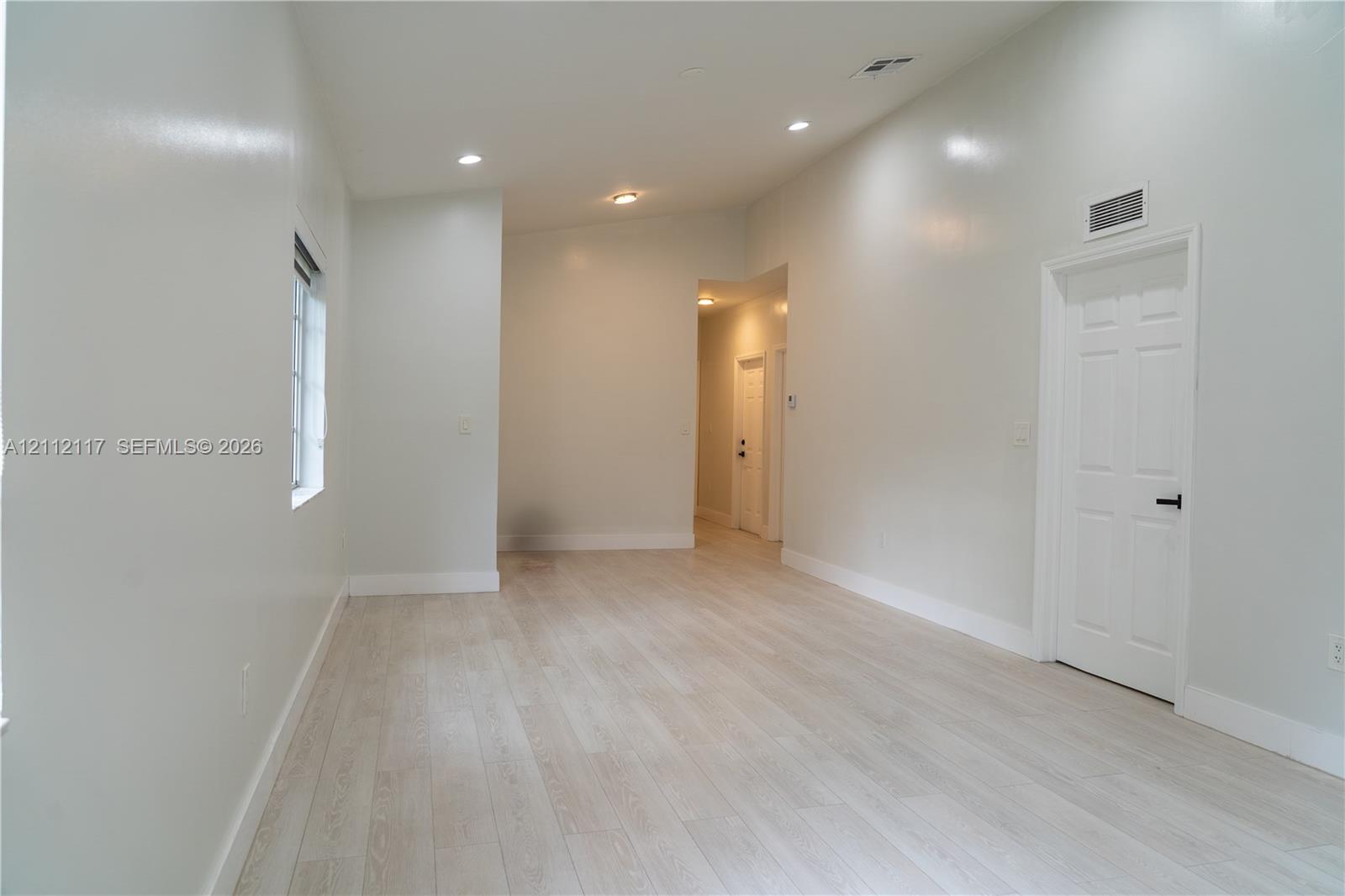 Interior space featuring vaulted ceilings, wood-finish flooring, recessed lighting, and a six-panel door with matte black hardware Interior space featuring vaulted ceilings, wood-finish flooring, recessed lighting, and a six-panel door with matte black hardware