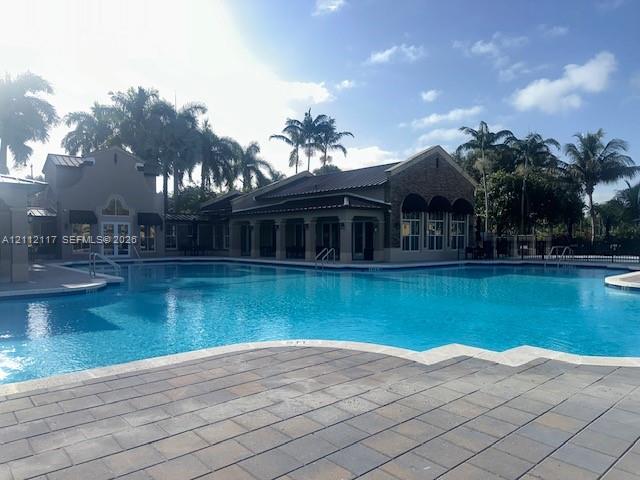 Large swimming pool featuring stone-paver decking, metal roof architecture, stone veneer accents, and covered poolside lounging areas
