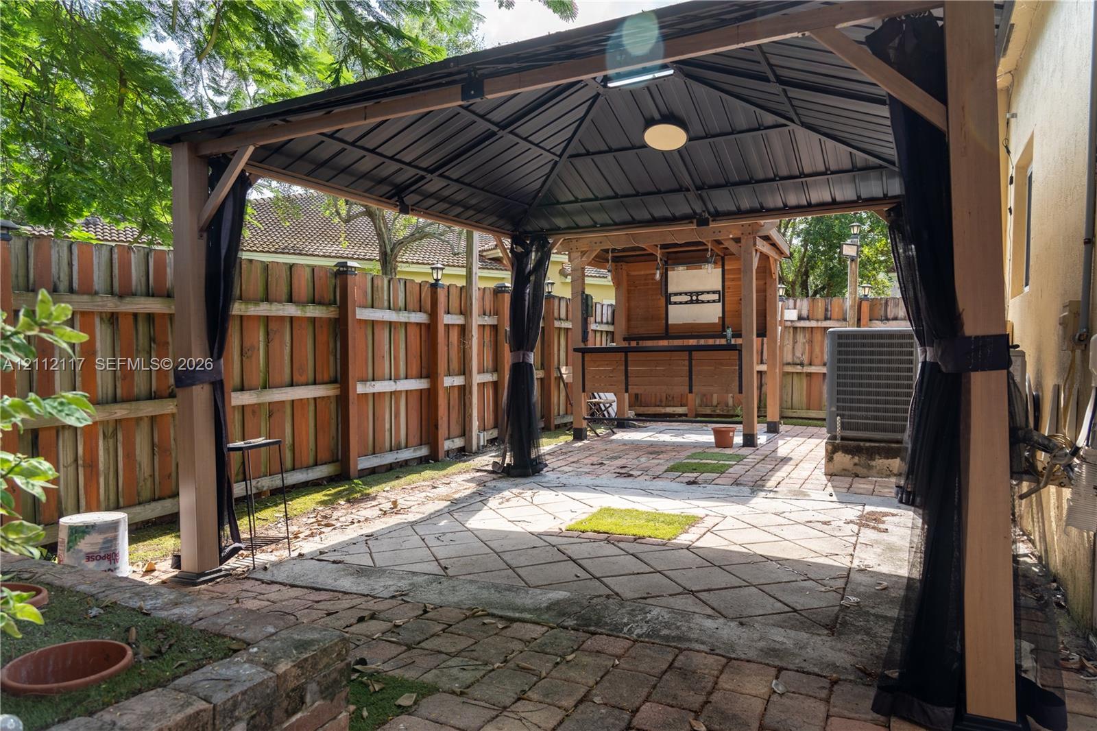 Covered outdoor structure with a metal roof, wood-frame bar, paver patio, and privacy fencing