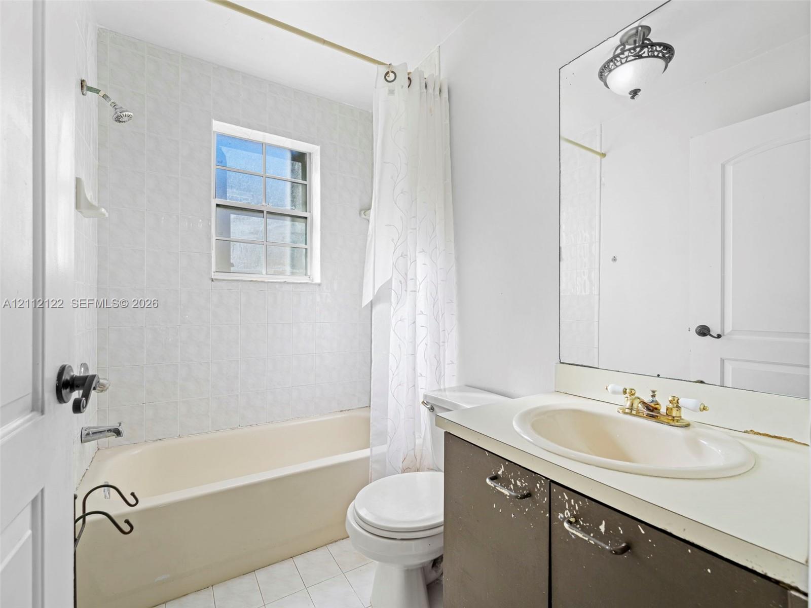 Full-width wall mirror, bathtub with a tiled surround, recessed window, and vanity with an integrated basin and metallic finish hardware