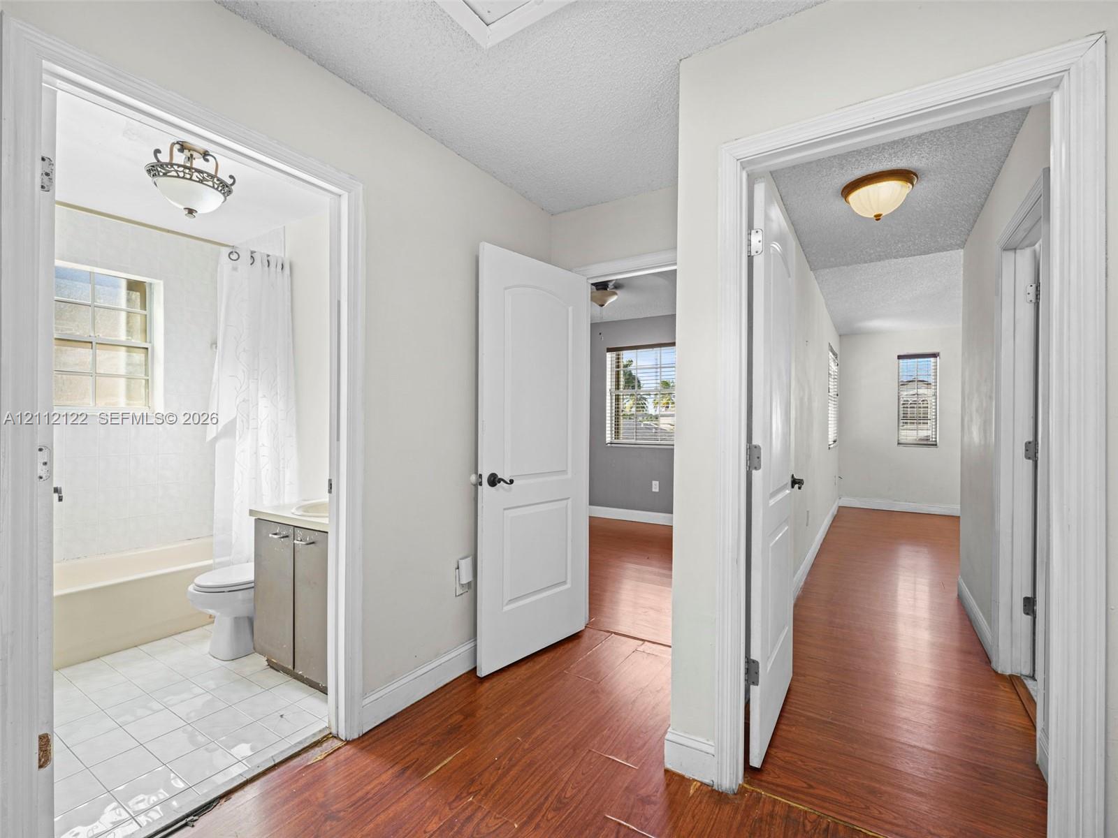 Interior hallway featuring wood-finish flooring, two-panel interior doors with oil-rubbed bronze hardware, and tile flooring within the restroom area