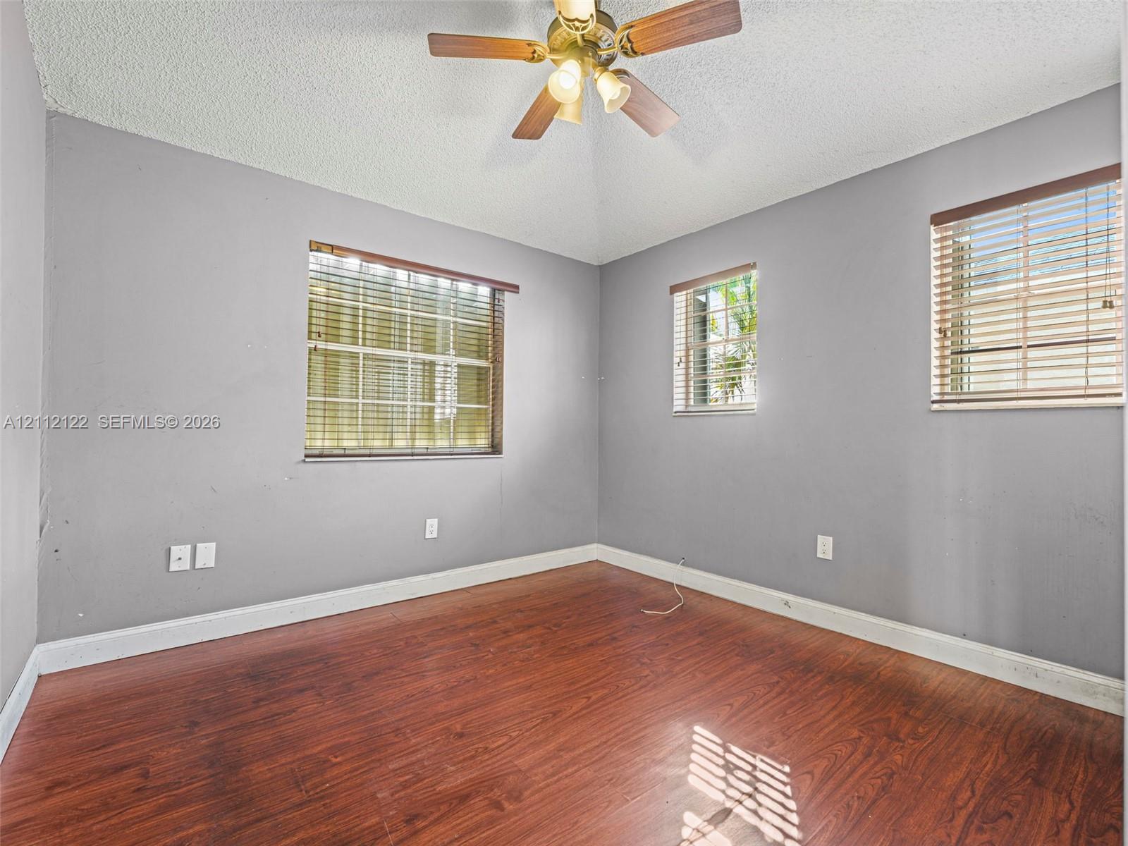 Room featuring wood-finish flooring, vaulted ceilings, a central multi-bulb ceiling fan, and windows equipped with horizontal blinds