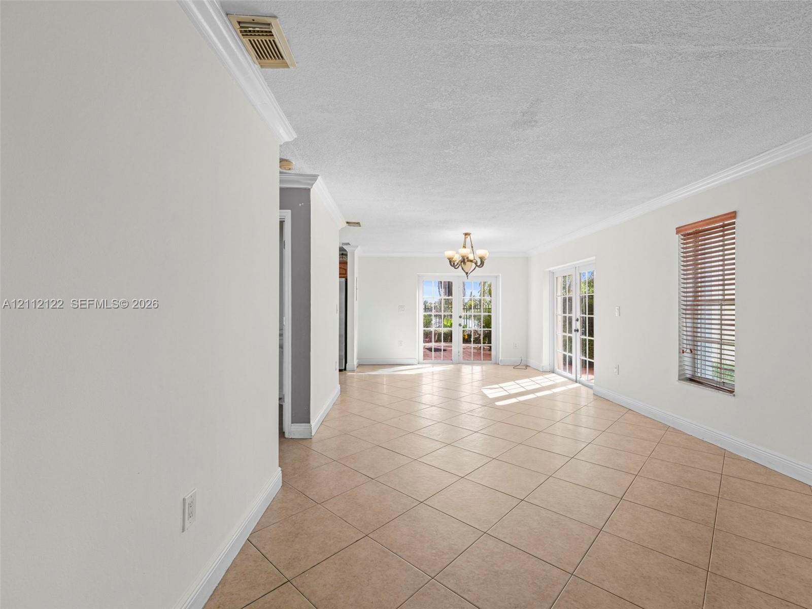 Neutral-toned interior featuring ceramic tile flooring, crown molding, multi-light chandelier, and dual sets of glass-paned French doors