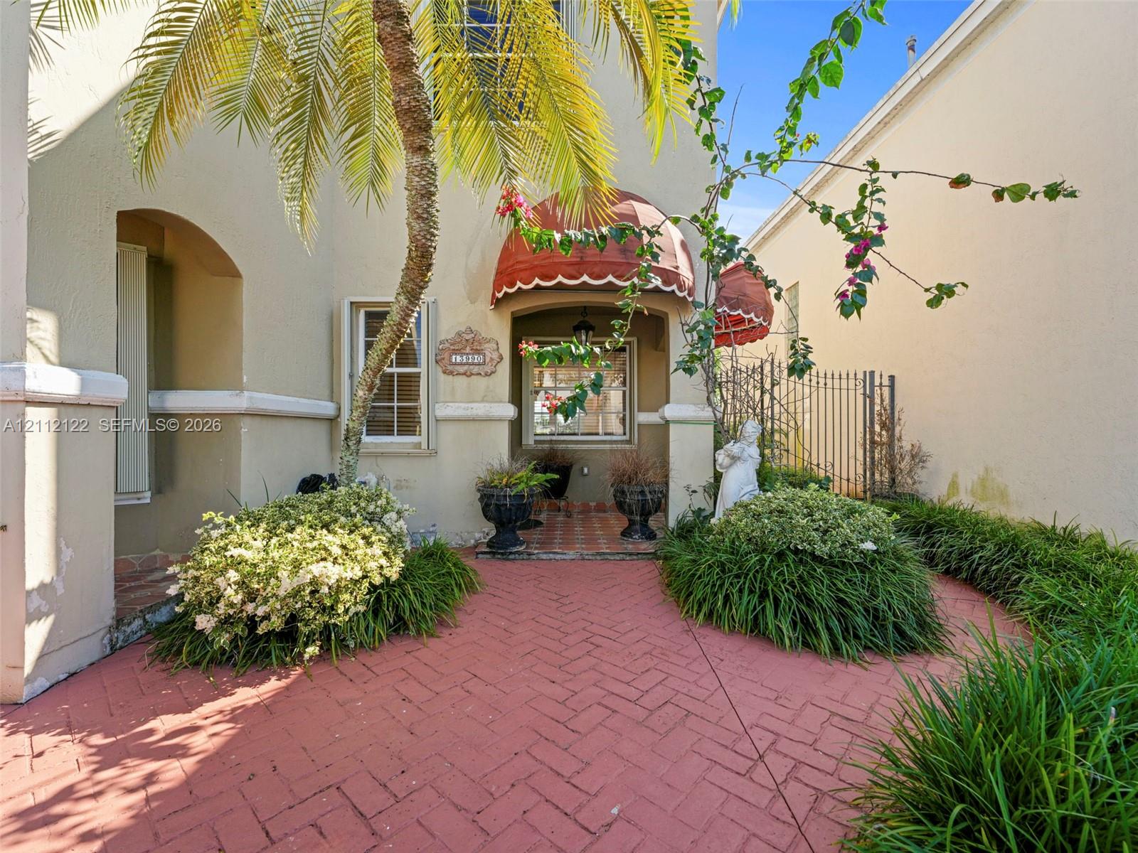 Stucco exterior featuring a covered entryway, red brick herringbone-patterned pavers, decorative canvas awnings, and multi-paned windows