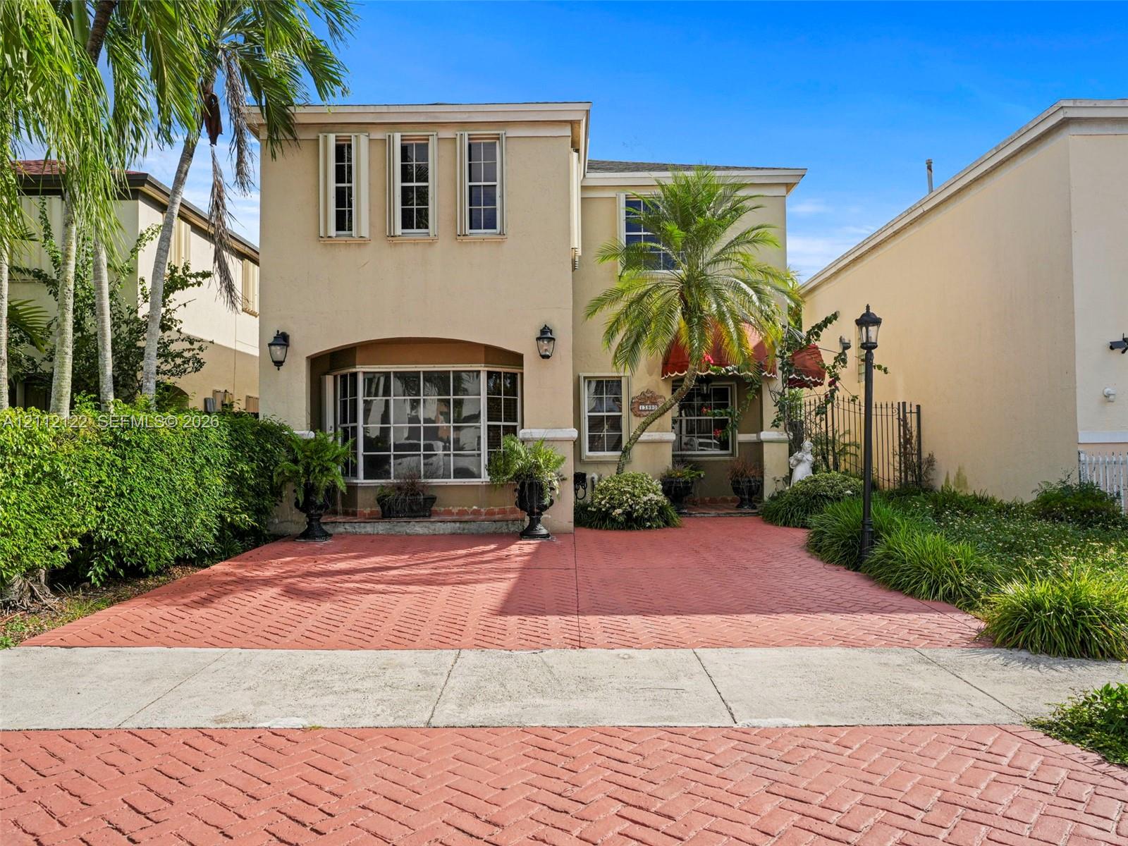 Two-story exterior featuring a stucco faade, herringbone-patterned paved driveway, bay window, and arched entryway with decorative awning