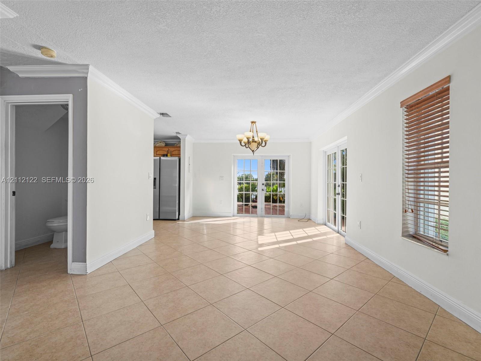 Open interior space featuring light-toned tile flooring, crown molding, a multi-arm chandelier, and two sets of glass-paned doors
