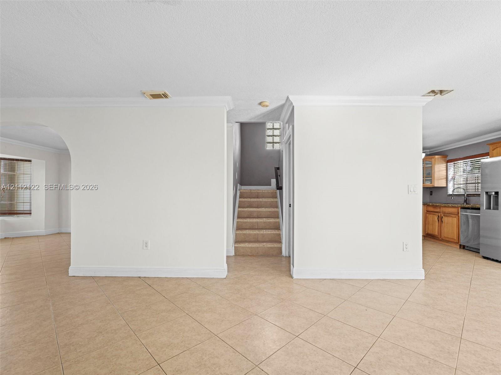 Neutral-toned tile flooring, arched architectural opening, staircase with carpeted treads, and crown molding